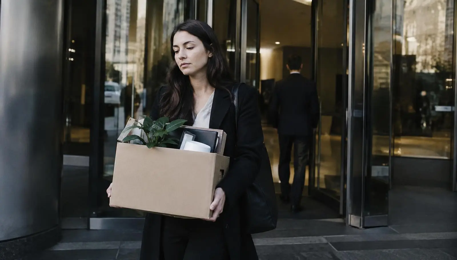 Employee leaving an office building with a box of belongings